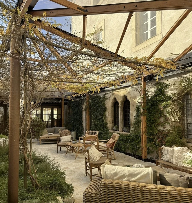 Terrasse couverte d'une pergola en bois avec vignes, mobilier en rotin naturel disposé sur dallage pierre
