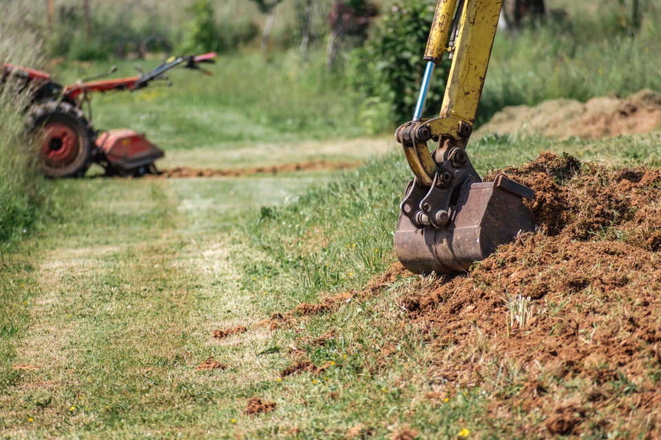 Chantier de construction extérieur avec pelleteuse jaune en action, opérateur dans la cabine, excavation de terre et matériaux